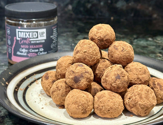 nut butter cocoa truffles stacked on a plate with a jar of nut butter in the background