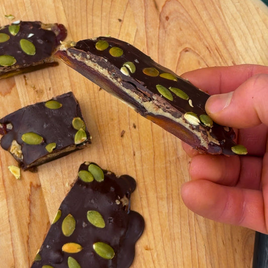 Homemade chocolate date bark with a chewy Medjool date base, creamy nut butter filling, and a snappy dark chocolate coating, topped with crunchy pumpkin seeds. A no-bake, healthy treat inspired by date Snickers.