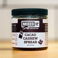 A jar of Cacao Cashew Spread on a kitchen counter, with the label 'MIXED UP Craft Nut Butter' and the product name clearly visible.